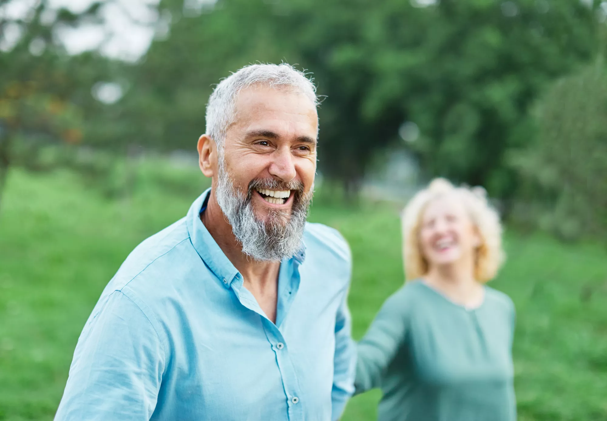 Smiling couple holding hands and walking in a field.